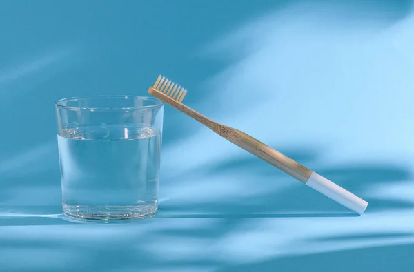wooden toothbrush and glass with water on a blue background