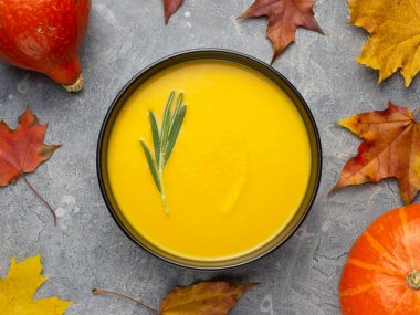 Akçaağaç yaprakları ve balkabağı parçalarıyla gri beton yüzeyde balkabağı çorbası manzarası