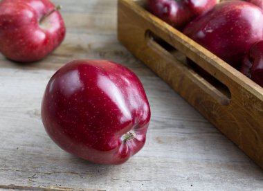 Ahşap bir kırsal masada olgun kırmızı bir elma. Arkaplanda elmalar olan tahta tepsi
