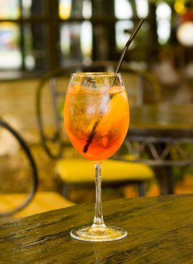 Bir bardak buzlu aperol spreyi, portakal dilimi ve kokteyl kamışı. Lokantadaki ahşap masada bir bardak ferahlatıcı kokteyl.