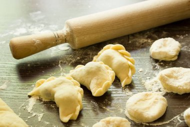 Three dumplings stuffed with cherries on the table next to a rolling pin and dough blanks for dumplings. Traditional summer dumplings in Ukrain