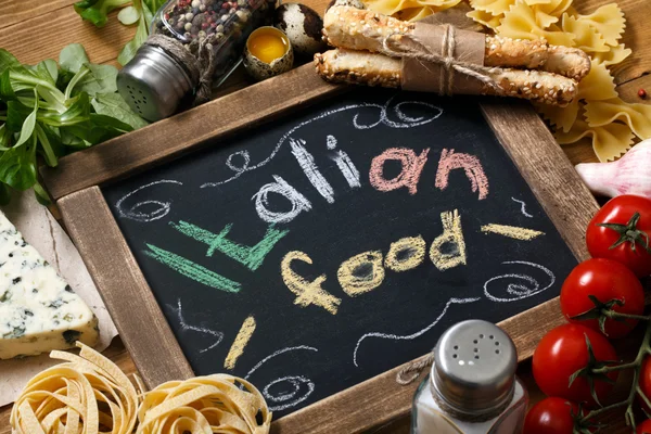 Italian food on vintage wood background with chalkboard — Stock Photo, Image