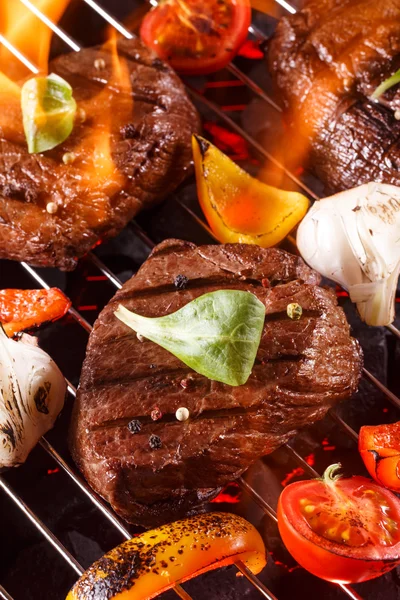 Bife de carne em uma churrasqueira com chamas com legumes — Fotografia de Stock