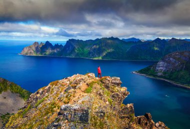 Hiker standing on the top of Husfjellet Mountain on Senja Island in Norway clipart