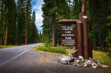 Welcome sign at the entrance to Crater Lake National Park in Oregon, located along the Volcanic Legacy Scenic Byway in a dense forest.