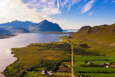 Aerial view of a road going through Lofoten Islands in Norway with mountains, village and lake.
