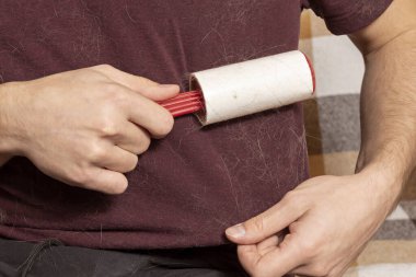 Yapışkan elbiseli bir adam kıyafetlerinden hayvan tüyü çıkarır. Kıyafetlerde kedi tüyü. Kedi tüylerini yokeden yapışkan bir silindir. tüy temizleme aracı.