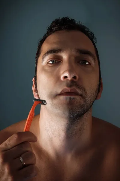 A tanned man shaves his face. Orange shaving machine. Half of the face is shaved. Facial skin care.