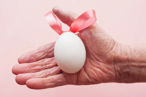 Mano Una Anciana Sosteniendo Huevo Blanco Con Cinta Rosa Forma — Foto de Stock