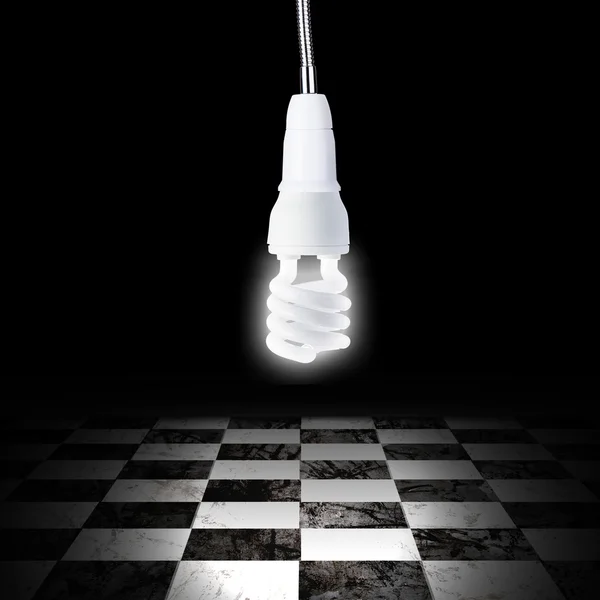 Light bulb in empty room with black and white checker floor — Stock Photo, Image