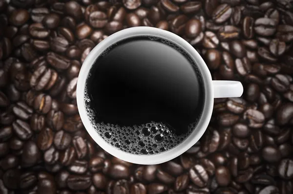 Kopp hett kaffe på kaffebönor bakgrund — Stockfoto