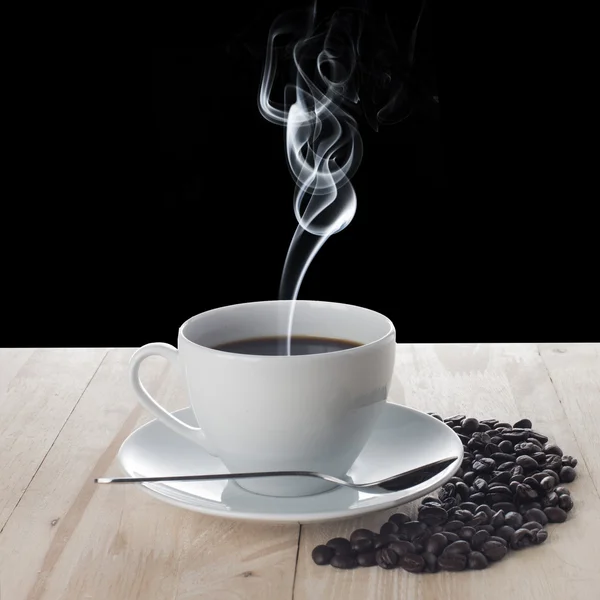 Varm kopp kaffe och kaffebönor på bord av trä — Stockfoto