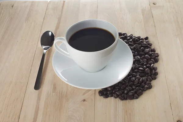Varm kopp kaffe och kaffebönor på bord av trä — Stockfoto