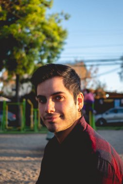 Yakışıklı, genç ve mutlu beyaz bir adam. Parkta gülümsüyor. Gün batımının ışığı yüzüne vuruyor.