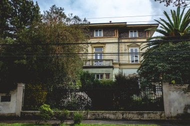 Eski terk edilmiş üç katlı taş ve tuğlalı ev balkon, süs, ağaçlar ve palmiyeler bulutlu bir günde, Valdivia, Şili