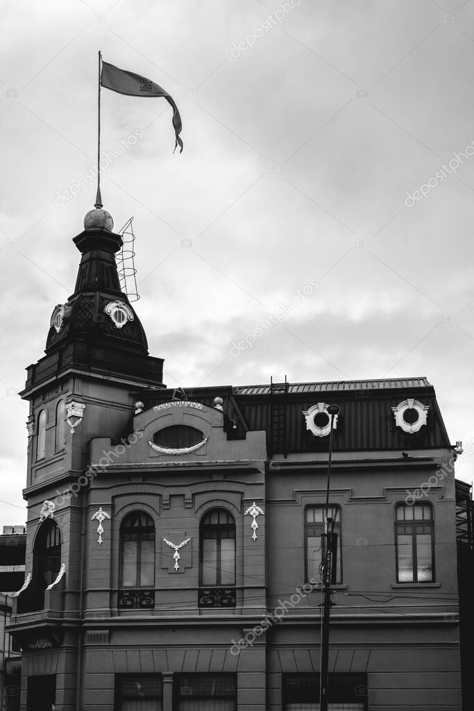 Beautiful old centuries five stored building with neoclassical architecture, ornaments, sculptures, flag and domes in a cloudy day, Valdivia, Chile (in black and white)