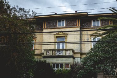 Eski terk edilmiş üç katlı taş ve tuğlalı ev balkon, süs, ağaçlar ve palmiyeler bulutlu bir günde, Valdivia, Şili