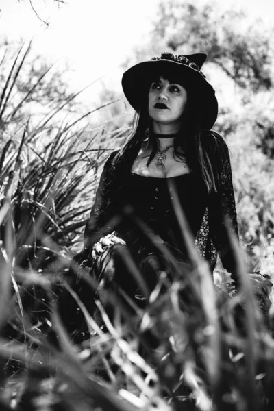 黒の釘やアクセサリー 魔法の木製の杖と自然の間の森の中で魔女の帽子と様式化された手から美しい若い ゴシック セクシーと魔女の女性 黒と白で — ストック写真