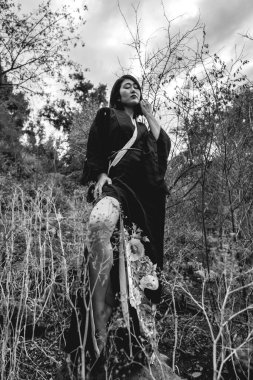 Genç ve seksi Japon kadın portresi. Çiçekli, geleneksel siyah bir kimonosu var. Güz ormanındaki büyük bir kayanın üzerinde bacaklarını ve ayaklarını gösteriyor.)