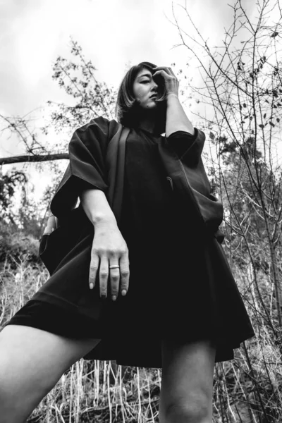 在秋天的森林里 性感而年轻的日本女人穿着美丽的老式传统黑色和服 在一块大岩石上摆出姿势并露出腿的画像 黑白相间 — 图库照片