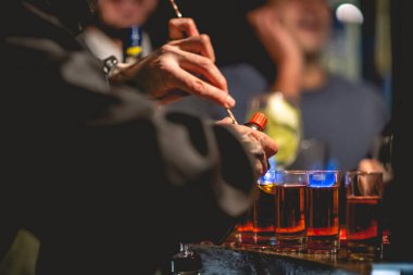 Barmen elleri biraz 'alevli doktor biberi' hazırlıyor. Amparetto ve aperatiften yapılan geleneksel bir kokteyl. Ateşe veriliyor ve birayla birlikte bardağa atılıyor.