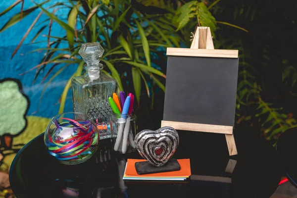 小さな黒板 色のペン 色の紙 リボン ガラス瓶と庭でラテン語の結婚式で植物の背景と小さな心の装飾を持つメッセージのための丸テーブル — ストック写真