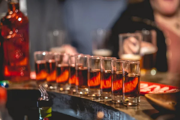 Line of shot glasses with a half of orange appetizer and a bottle in the bar from a pub