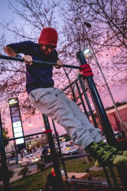 Formda ve güzel ve renkli günbatımı gökyüzü olan bir sokak çalışma parkında spor yapan, yün şapkalı, spor yapan yakışıklı ve atletik Latin bir adam.