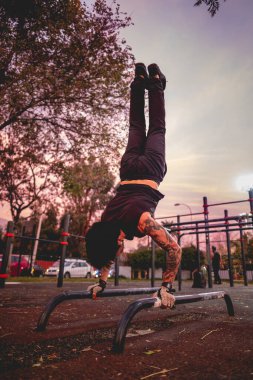 Güzel dövmeleri, siyah giysileri ve spor eldivenleri olan sağlıklı ve formda genç bir Latin adam güzel ve renkli günbatımı gökyüzü olan bir parkta spor yapıyor.