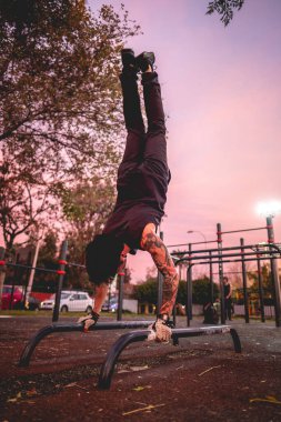 Güzel dövmeleri, siyah giysileri ve spor eldivenleri olan sağlıklı ve formda genç bir Latin adam güzel ve renkli günbatımı gökyüzü olan bir parkta spor yapıyor.
