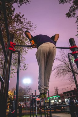 Formda ve güzel ve renkli günbatımı gökyüzü olan bir sokak çalışma parkında spor yapan, yün şapkalı, spor yapan yakışıklı ve atletik Latin bir adam.