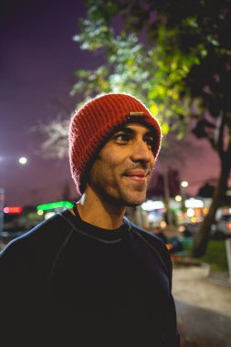 Gülümseyen, sağlıklı, yakışıklı ve spor parkında güzel ve renkli günbatımı gökyüzü olan yün şapkalı genç bir Latin 'in portresi.