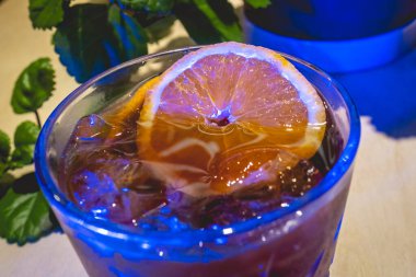 Kapalı kapılar portakal suyu, soğuk kahve ve yeşil dekoratif bitkilerle gecenin karanlığında bir kafede neon mavi ışıkla.