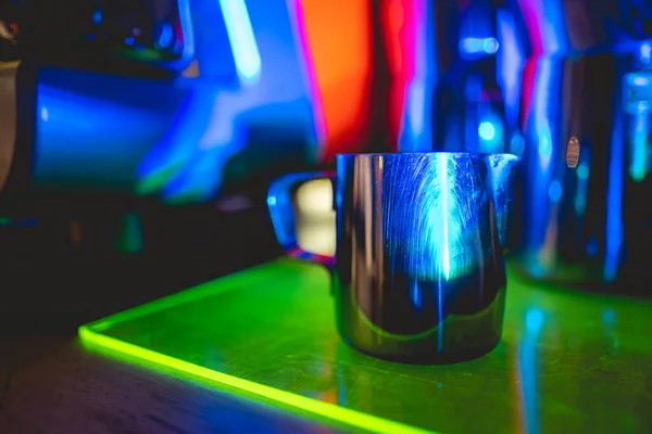 Vintage coffee machine and barista metallic milk jug over a neon green tray in a coffee shop interior in the night with dark blue lights