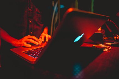 Geceleri kırmızı ışıkların altında Apple MacBook dizüstü bilgisayarı kullanan bir adamın elleri