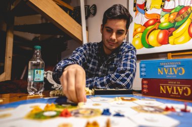 'Denizciler' genişleme 'den bir' Catan 'masa oyunu parçası tutan güzel beyaz el ve iç ışık gömlekli genç adam yakın plan