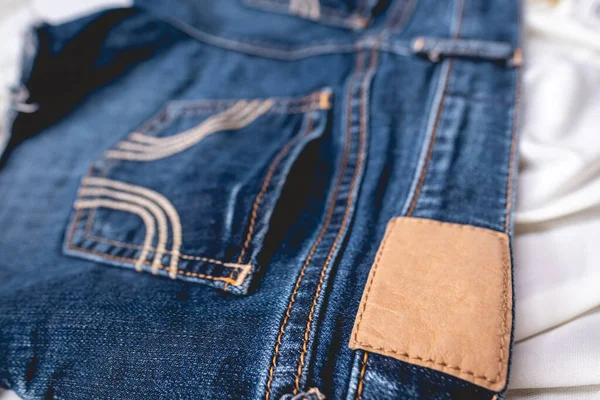 Belt and label detail of fashion blue jeans shorts over wrinkled white sheet