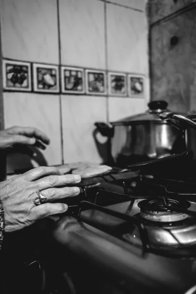 Beautiful hands of elderly latino woman cooking on traditional kitchen stove with gas burners with traditional toaster with \'sopaipillas\' (fried pastry) and pots (in black and white)