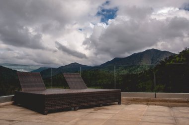 Rustic sun loungers in a rooftop with view of landscape in with forest, mountains and cloudy sky 