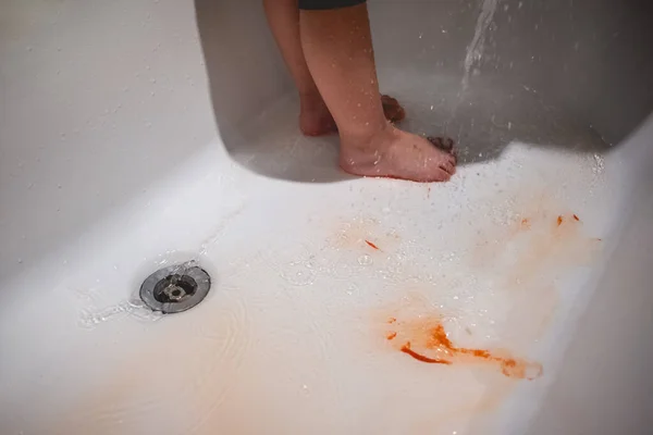 Feet and legs of a little girl with orange paint being washed with water in a white tub