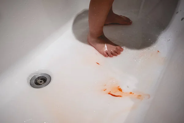 Feet and legs of a little girl with orange paint being washed with water in a white tub