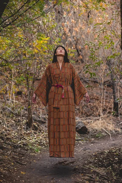 Paranormal portrait of sexy and young japanese woman with beautiful old traditional brown and orange kimono floating in the autumn forest