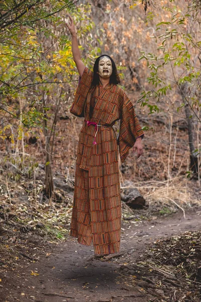 Paranormal portrait of sexy and young japanese woman with beautiful old traditional brown and orange kimono and traditional noh mask floating in the autumn forest