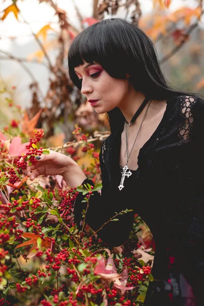 Young and skinny hispanic goth girl with black dress in the autumn forest with red, orange and yellow dry leaves