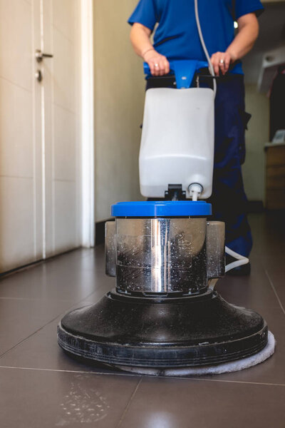 Young latino janitorial worker lady in blue uniform cleaning in building with industrial vacuum cleaner