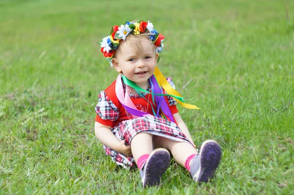 A little girl with a wreath on his head sitting in the grass — Stock Photo, Image