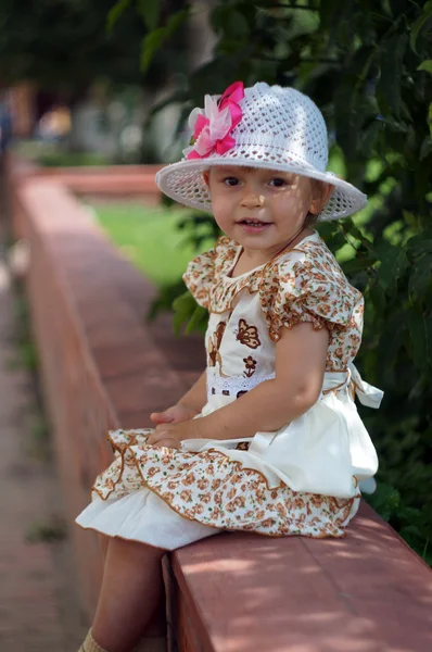 Chica de dos años con un vestido elegante y sombrero sentado en la calle —  Fotos de Stock