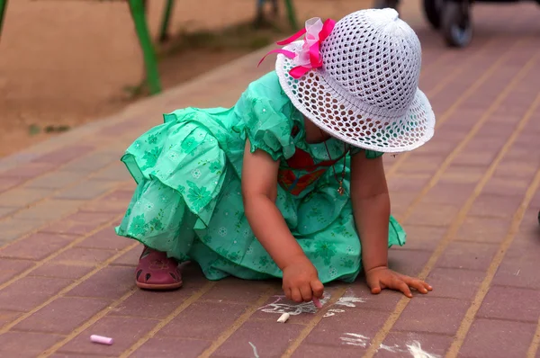 Twee-jaar-oude meisje trekt een krijt op de straat Stockfoto