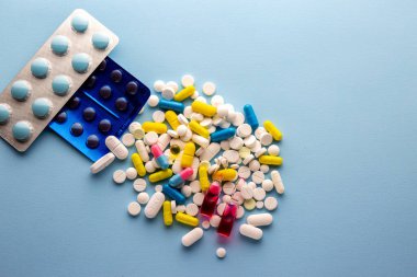 Aşırı dozda hap. İlaçlar. Çok renkli haplar ve ilaçlar. İlaçların geçmişi. Grip tedavisi. Coronavirus tedavisi. Eczane. Kamu alanındaki ilaçlar. Vitaminler. - Uyuşturucu. Mavi arka planda renkli terlikler. Soğuk algınlığı tedavisi