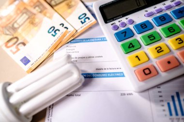 İspanya 'da aylık elektrik tüketiminin yakın çekimini yapın. Olay yerinde ampul, hesap makinesi ve avro nakit para vardı. Konsept: ekonomik enflasyon